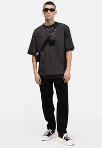 Sort mesh t-shirt med logo, parret med sorte afslappede bukser og sorte sneakers med hvid sål. Inkluderer solbriller og en lille crossbody taske.
