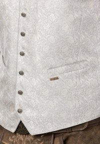 Hellgraue, gemusterte Weste mit floralem Design, silbernen Akzenten und dekorativen Knöpfen. Verfügt über eine einzelne Tasche und ein Logoschild.