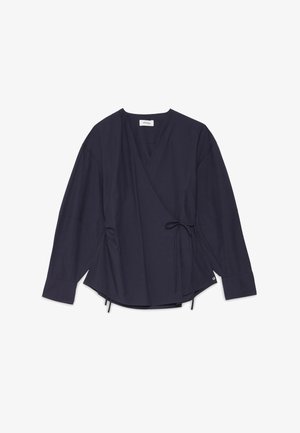 Blouse cache-cœur bleu marine à manches longues avec col en V, lien ajustable sur le côté et poignets boutonnés, posée à plat sur fond blanc.