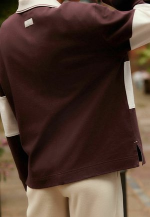 Polo shirt bordeaux con pannelli laterali bianchi, maniche corte e colletto. Include un piccolo etichetta sul retro e spacco ai lati dell'orlo.