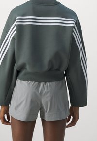 Mörkgrön sweatshirt med vita sidostänger, i kombination med ljusgrå shorts. Avslappnad passform med ribbad manschett och nederkant.