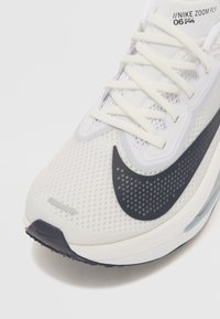 Nike Zoom Fly tenisice za trčanje, s bijelim mrežastim gornjim dijelom, crnim akcentima, teksturiranim materijalom i elegantnim dizajnom s vidljivim sustavom vezanja.