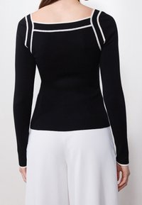 Haut noir en maille avec un décolleté carré et des accents blancs aux épaules et aux bras, doté de manches longues et d'une silhouette ajustée.