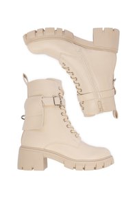 Botine de luptă bej la glezna, cu toc gros, șnururi, fermoar pe lateral, curea cu cataramă și un mic pouch atașat pe partea exterioară.