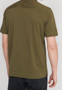 Olivgrön, kortärmad skjorta gjord av mjukt bomullsmaterial. Har en klassisk krage och en ren, minimalistisk baksidesdesign.