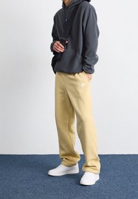 Grå hoodie med en framficka, kombinerad med ljusgula träningsbyxor med en vit Nike-logotyp och vita sneakers. Enkel, avslappnad design.