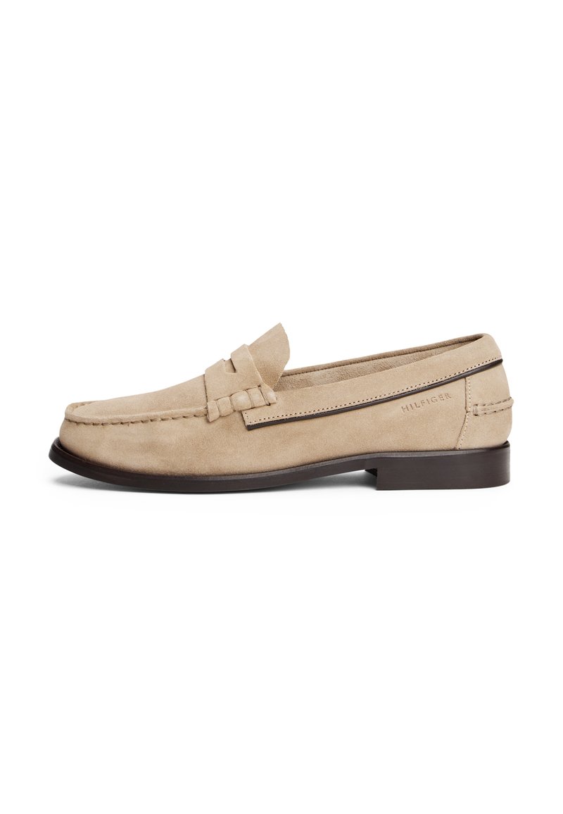 Beige semskede mokkasiner med en sydd design, en detalj med frontbånd, og en mørk brun såle. Har "HILFIGER"-logoet preget på siden.