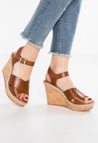 Sandali wedge in pelle marrone con tacco in sughero, dotati di cinturini incrociati, fibbia alla caviglia e dettaglio decorativo in corda lungo la suola.