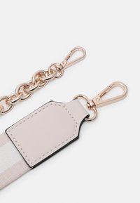 Svetle růžový kožený pásek s metalicky zlatým řetězem, obsahující dva zlaté karabinkové uzávěry a obdélníkovou tag s černými okraji.