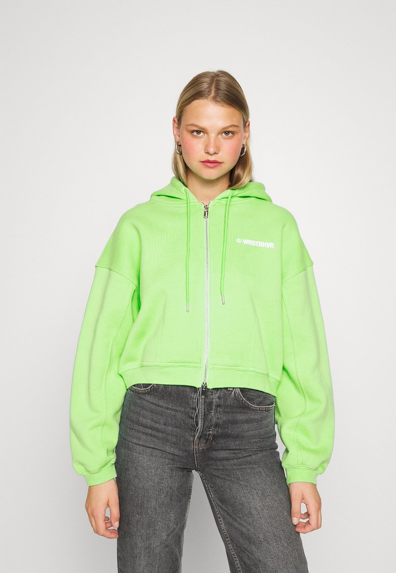 Sweatshirt com capuz cortado em verde neon brilhante, com fecho frontal de zíper e mangas oversized. Logotipo da marca impresso em branco.
