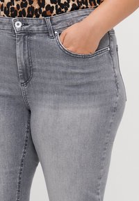 Grå denimjeans har en medelhög passform, femfickorsdesign och en slät textur med subtila blekningar på framsidan.