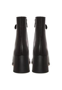 Paire de bottines en cuir noir avec talons carrés vues de dos sur fond blanc.