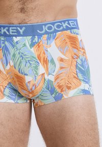 Boxer da uomo con elastico blu e logo "Jockey", realizzati in tessuto leggero, decorati con un vivace motivo di foglie tropicali in arancione e verde.