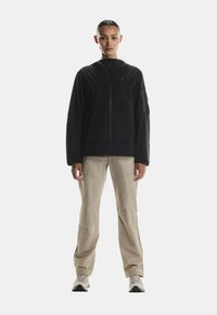 Czarna kurtka na zamek o gładkiej fakturze, z długimi rękawami i kieszeniami po bokach, zestawiona z beżowymi spodniami cargo oraz jasnymi trampkami.