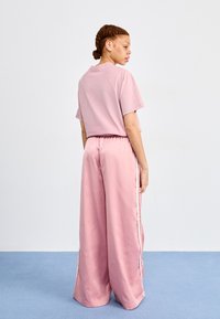 Rosa oversized t-shirt med korta ärmar, parat med vida rosa byxor med sidostrickor. Slät textur, avslappnad design.