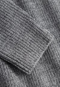 Gray knitted sweater fabric with a ribbed texture. Visible stitches and overlapping sections create depth and pattern detail.