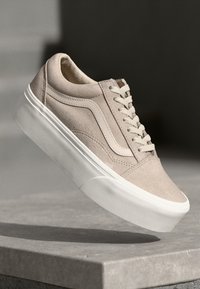 Beige semskinn-sneakers med hvit gummisåle, med snøring og detaljer på siden; lavt design med rund tå.