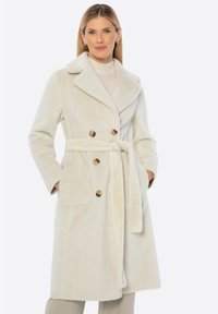 Abrigo crema de doble botonadura con grandes botones marrones, cinturilla ajustada y cuello con muesca, hecho de una suave tela texturizada.