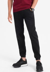 Svarta joggerbyxor i denim, med resårmidja och avslutade nederkanter. Bärs tillsammans med svarta sportskor.