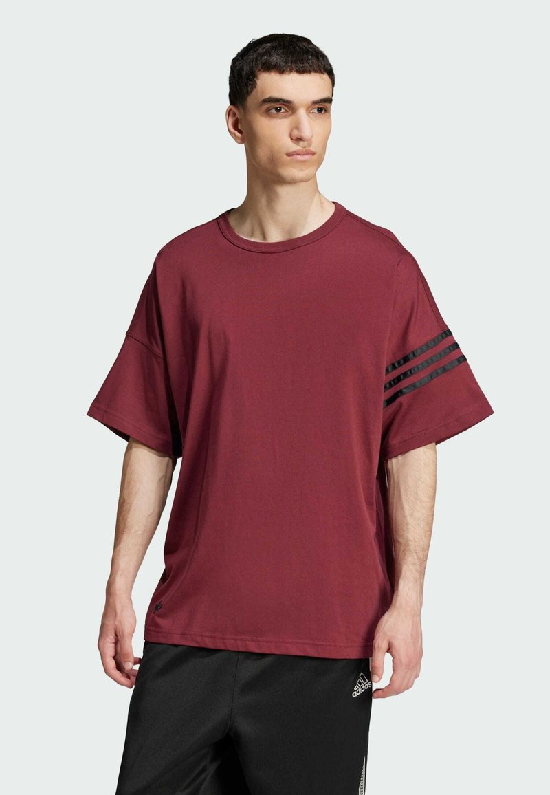 Bordo oversize majica izrađena od pamuka, s okruglim izrezom, kratkim rukavima i tri crne pruge na lijevom rukavu.