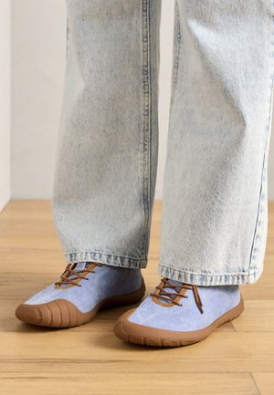 Light blue suede shoes with brown rubber soles and laces. Rounded toe design with stitching accents. Worn with relaxed fit light blue jeans.