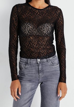 Schwarzes Langarmoberteil mit einem durchsichtigen Leopardenmuster und Rundhalsausschnitt. Kombiniert mit grauen, hoch taillierten Jeans aus Denim.