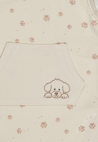 Beige fabric with brown puppy paw prints and a small pocket featuring an embroidered puppy face with ears and paws.