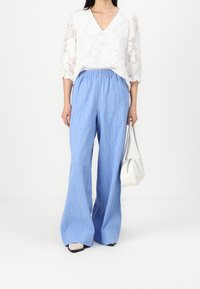 Vit blommig spetsoberdel med V-ringning, i kombination med ljusblå, vida byxor i krinklat tyg. Accessoarer med en liten vit handväska.