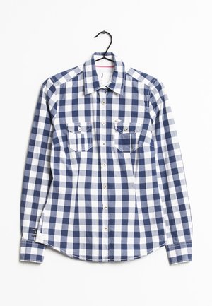 Camisa de manga larga con estampado a cuadros en azul y blanco, con dos bolsillos en el pecho, exhibida en una percha negra contra un fondo blanco.