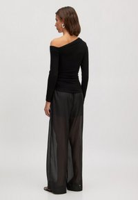 Zwart langemouwen top met een asymmetrische halslijn, gecombineerd met doorschijnende zwarte wijde broek. Glad materiaal met een getailleerde pasvorm.