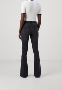 Black flared jeans with a high waist, featuring back pockets and a smooth denim texture. Worn with a white ribbed short-sleeve top.