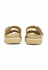 Sandalias marrones con diseño de espalda abierta, correas ajustables y herrajes plateados. Suelas gruesas y texturizadas con una franja de acento blanca.