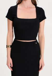 Czarny prążkowany krótki top z kwadratowym dekoltem i krótkimi rękawami, w połączeniu z pasującą spódnicą z bocznym akcentem w postaci guzika.