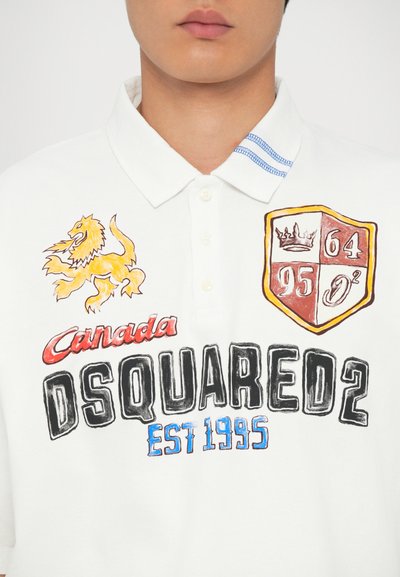 Tricou polo alb cu guler, având grafice brodate colorate: leu, scut, numele mărcii "DSQUARED2" și anul înființării "1995."
