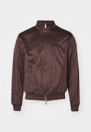 Brun bomberjakke lavet af skinnende stof med høj krave, frontlynlås, elastiske manchetter og livrem. Har minimal branding på brystet.