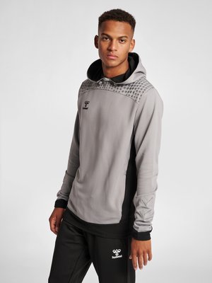 Lys grå atletisk hoodie med en sort accent, der har et mønstret skulderpanel og en kængurulomme. Sammen med sorte joggers.
