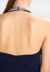 Mörkblå klänning med halterneck, dekorerad med glittrande detaljer, öppen ryggdesign och en diskret dragkedja.
