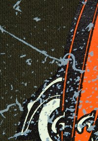 Teksturowany zielony materiał z białymi, pomarańczowymi i niebieskimi plamami, z wzorem w spirale i szczegółowym haftem.