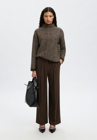 Rjavi pulover z vzorcem ribje kosti in visokim ovratnikom, rjave hlače z visokim pasom, črna torba tote z lokom in črni čevlji z ostrim koncem.