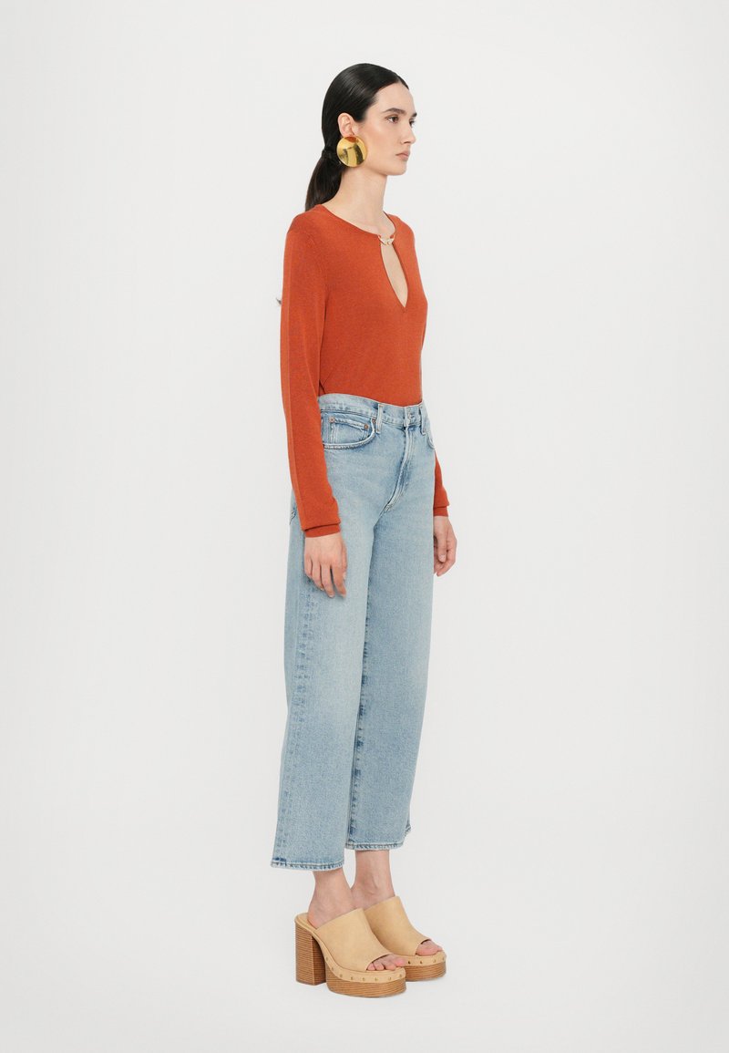 Rust long-sleeve top with a keyhole neckline, light blue high-waisted wide-leg jeans, and beige platform clogs with a wooden sole.