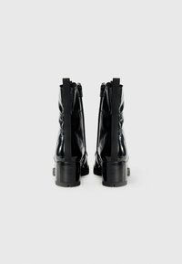 Botines de charol negro con tacón grueso, que cuentan con cremalleras laterales y acentos de tela texturizada. Acabado liso con un detalle mínimo.