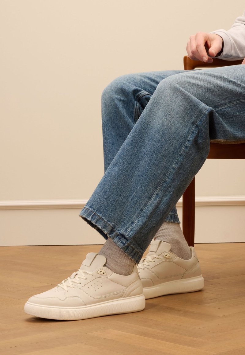 Crème leren sneakers met perforatiedetails en platte veters, gedragen met lichtblauwe denim, afgewerkt met een rafelige zoom.