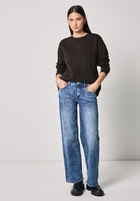 Un pull marron foncé avec un motif léopard, associé à un jean droit bleu clair et des bottes noires chunky.
