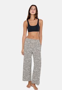 Top corto nero e pantaloni da pigiama bianchi con stampa leopardata marrone. I pantaloni hanno tasche e una vestibilità morbida. Il modello è a piedi nudi davanti a uno sfondo semplice.