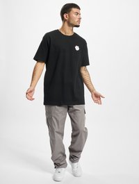 Sort bomulds t-shirt med et hvidt blomstermotiv på brystet, parret med grå cargo-bukser og hvide sneakers. Afslappet pasform, korte ærmer.