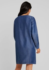 Denim-mekko, pitkät hihat, kauluksellinen kaula-aukko, tummansininen väri, puolipitkä, rento istuvuus, näyttää pehmeältä ja siinä on hieman kiiltoa.