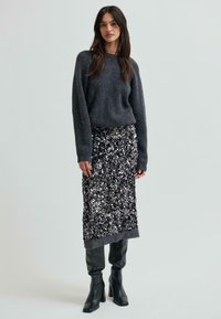 Szary, dzianinowy sweter z długimi rękawami w połączeniu z czarną spódnicą z cekinów do połowy łydki, dopełniony czarnymi, wysokimi botkami na obcasie.