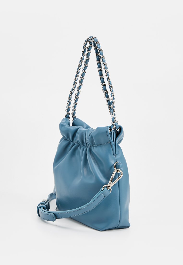 Sac à main en cuir bleu doux avec un haut froncé, des poignées en chaîne argentée et une bandoulière amovible avec un fermoir en métal sur fond blanc.