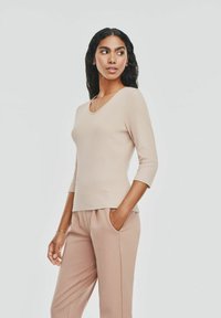 Jasno beżowa, prążkowana bluzka z długim rękawem, z okrągłym dekoltem i małym akcentem logo. Zestawiona z dopasowanymi luźnymi spodniami. Gładka faktura.
