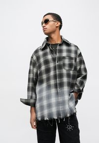 Μπλούζα σε υπερμεγέθη γραμμή με ασπρόμαυρο καρό σχέδιο από φανέλα, με τσέπη και ξέφτια στο τελείωμα, συνδυασμένη με μαύρο τζιν με φθορές.